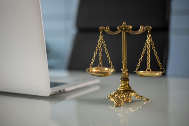 Golden justice scales on a desk beside a laptop, symbolizing law and balance